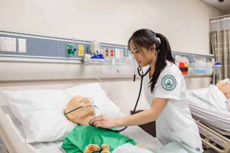 A nurse examines a synthetic patient in a hospital bed, showcasing hands-on training at Concordia University Irvine's ABSN program.
