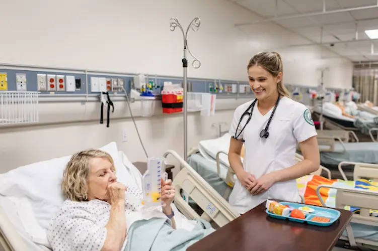 A nurse speaks with a patient in a hospital bed, reflecting the dedication of Concordia University Irvine ABSN students to patient care.