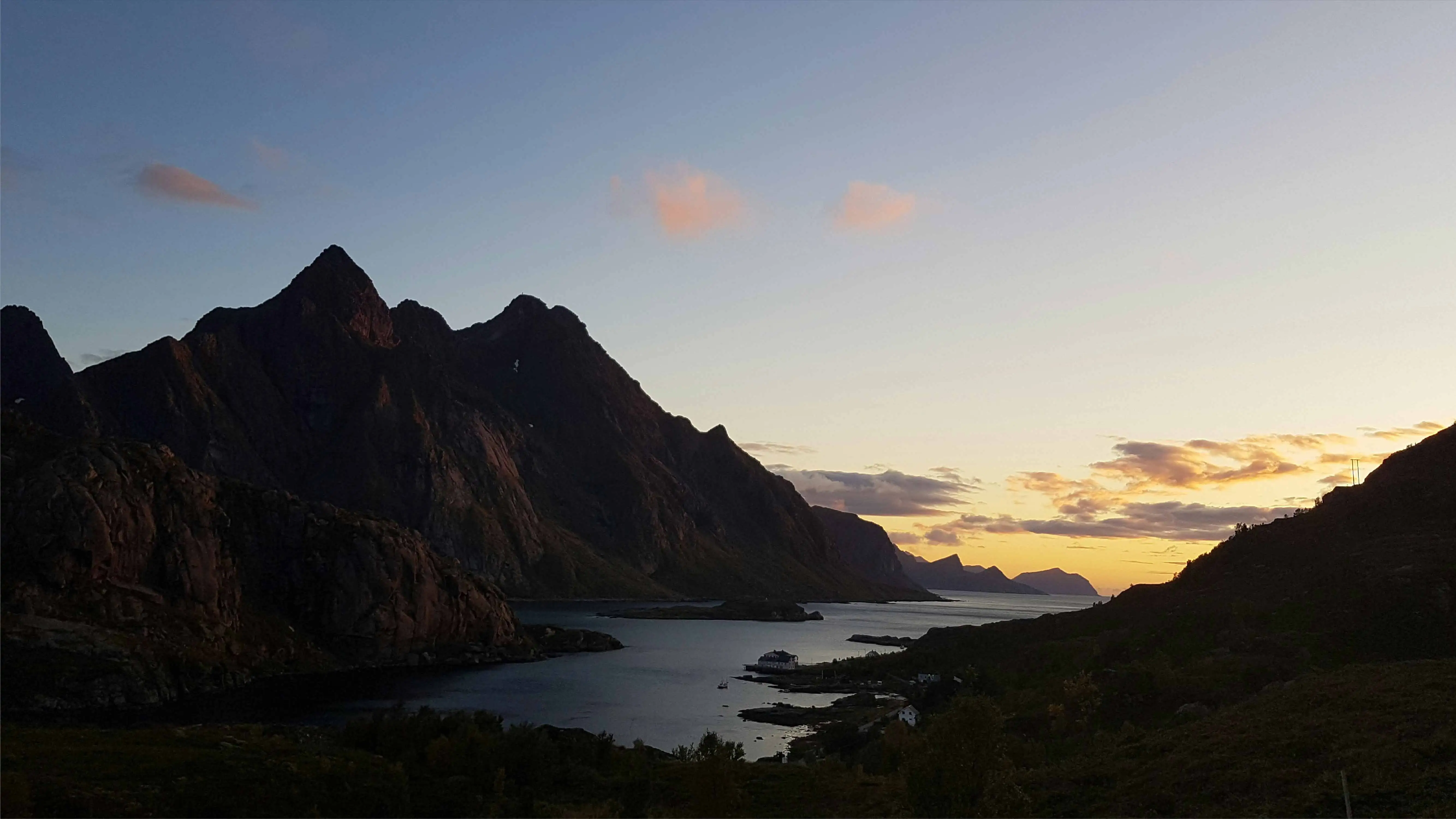 The sun sets dramatically over the Lofoten Islands, painting the sky with warm colors and reflecting on the serene waters below.