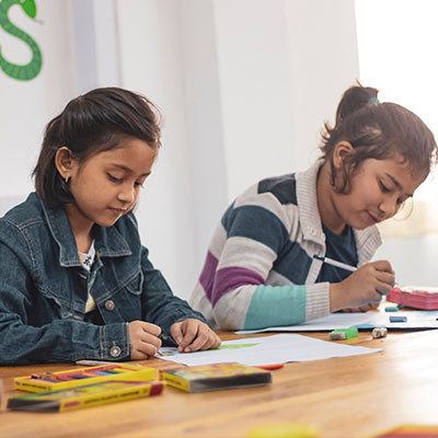 Two girls in a classroom writing.